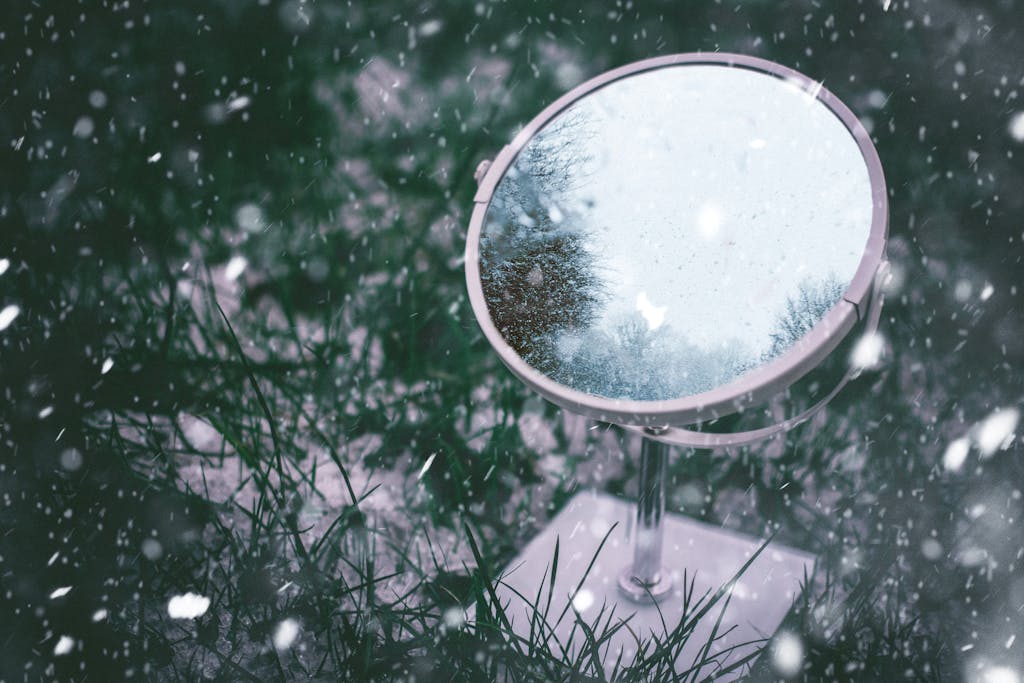 A mirror on snowy grass reflecting trees. Winter scene with falling snow.